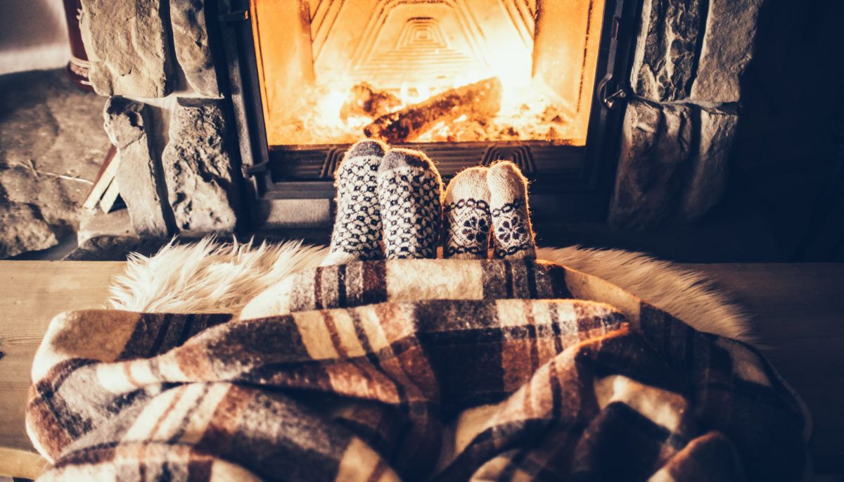 Two feet in socks and covered by a blanket in front of a fireplace