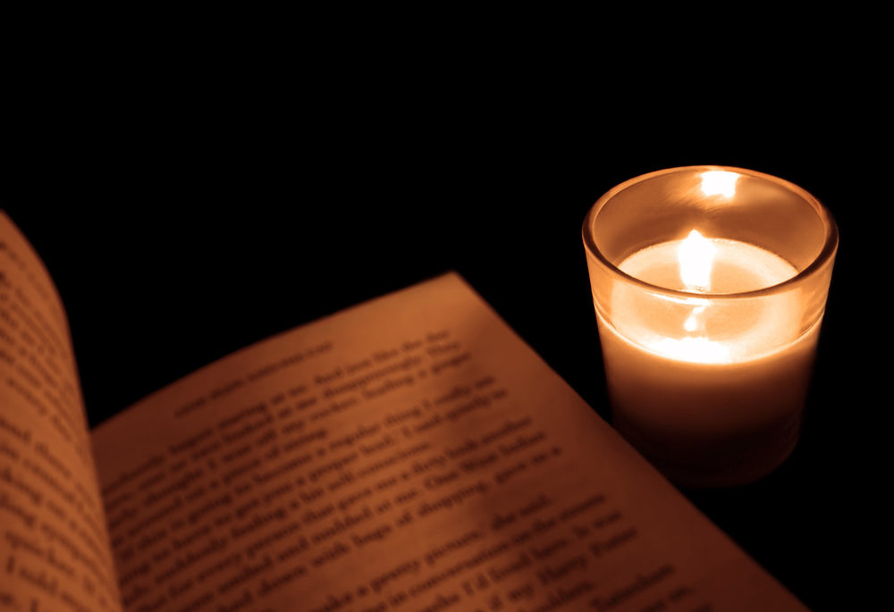 candle in glass holder beside a book
