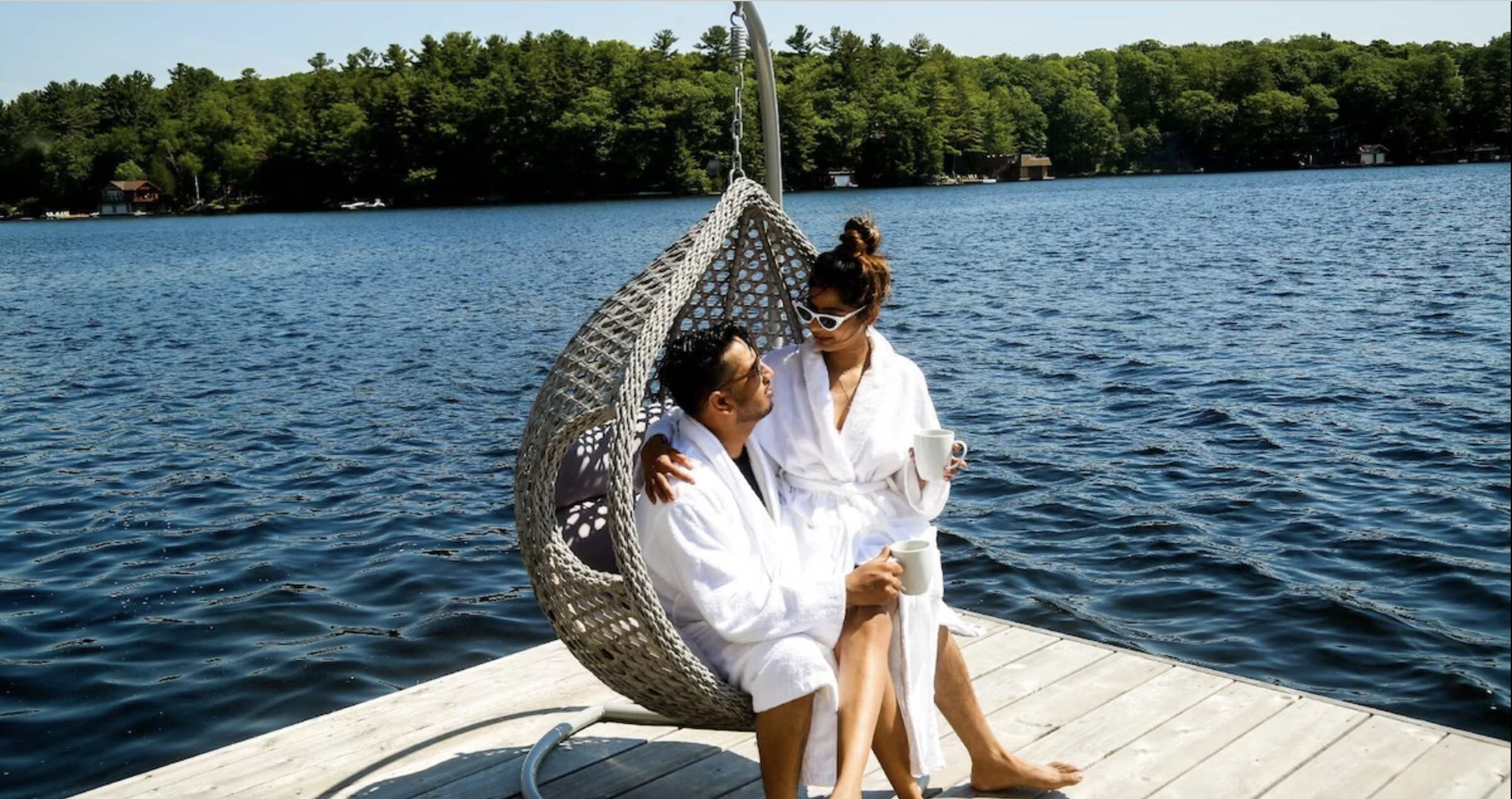 a couple sits in a swing chair on the dock in front of the lake