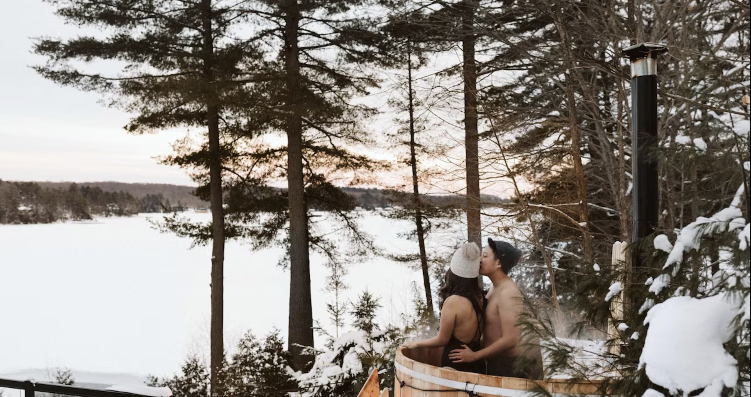 a couple embrace in the outdoor hot tub looking over the lake and pine trees