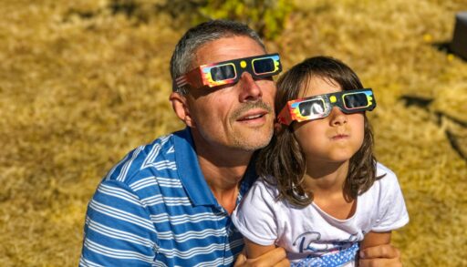 a man and young child watching the eclipse with eclipse glasses on